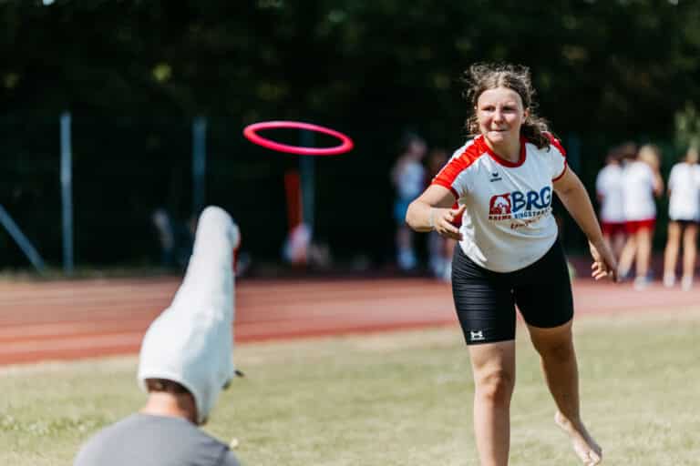 Mädchen wirft Ring auf Person mit Vogelkopf-Maske auf Sportplatz